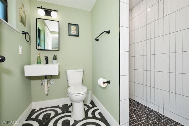 full bathroom with baseboards, toilet, a tile shower, tile patterned floors, and a sink