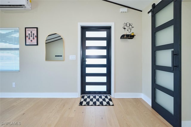 entrance foyer featuring a wall unit AC, a barn door, wood finished floors, and baseboards