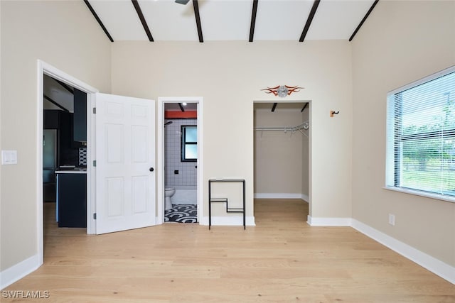 unfurnished bedroom with a spacious closet, light wood-style flooring, freestanding refrigerator, and baseboards