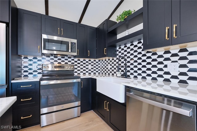 kitchen featuring open shelves, light countertops, decorative backsplash, stainless steel appliances, and a sink