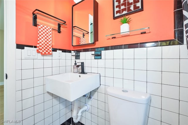 bathroom with tile walls, toilet, wainscoting, and a sink