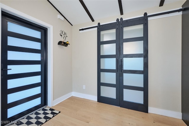 foyer entrance with a barn door, baseboards, light wood-style floors, and lofted ceiling