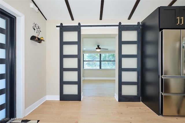 foyer entrance featuring a barn door, baseboards, light wood-type flooring, and ceiling fan