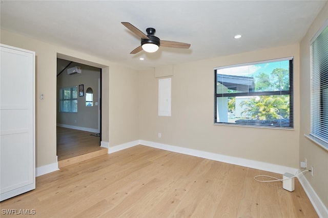 unfurnished room with a wall mounted air conditioner, baseboards, light wood finished floors, and ceiling fan