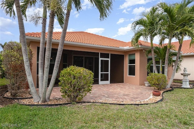 rear view of property with a tile roof, stucco siding, a yard, a sunroom, and a patio