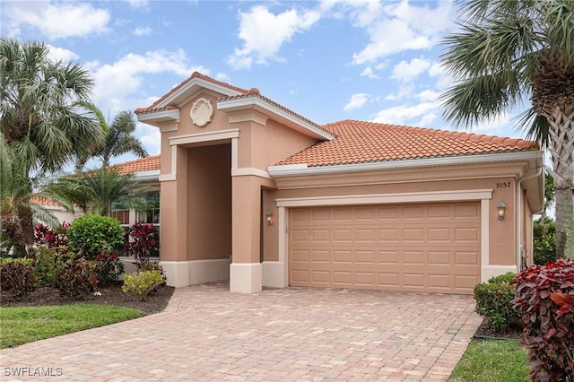 mediterranean / spanish house featuring decorative driveway, a tiled roof, an attached garage, and stucco siding