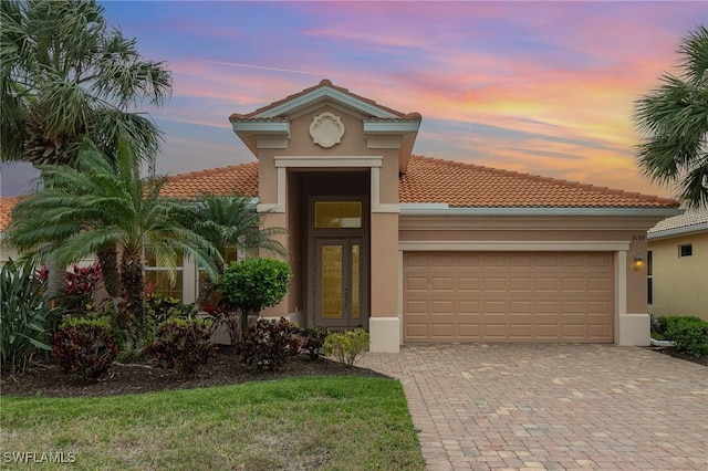 view of front of home featuring decorative driveway, a tile roof, an attached garage, and stucco siding