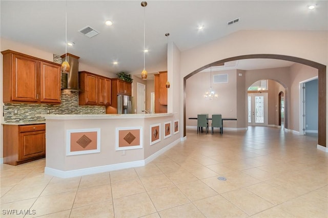 kitchen featuring visible vents, brown cabinets, stainless steel refrigerator with ice dispenser, arched walkways, and wall chimney range hood