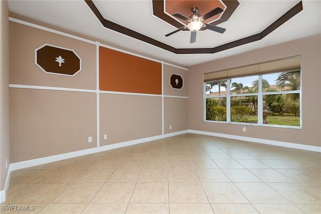 empty room featuring light tile patterned floors, baseboards, a ceiling fan, and a tray ceiling