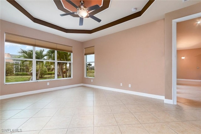 empty room with light tile patterned flooring, ceiling fan, baseboards, and a tray ceiling