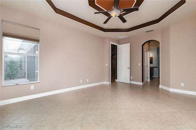 spare room with a tray ceiling, arched walkways, baseboards, and ceiling fan