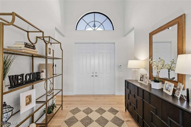 foyer entrance featuring baseboards, a high ceiling, and light wood-style flooring