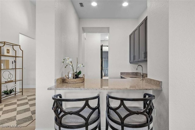 kitchen with a breakfast bar area, light stone countertops, visible vents, light floors, and a sink