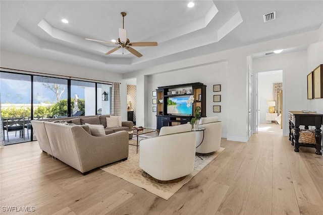 living room with a ceiling fan, baseboards, visible vents, a tray ceiling, and light wood-style flooring