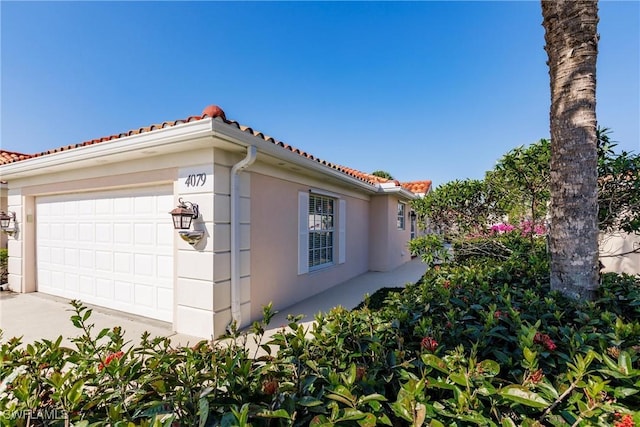view of side of home with a garage, a tiled roof, and stucco siding