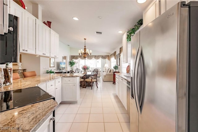 kitchen with light tile patterned floors, a peninsula, stainless steel appliances, white cabinets, and a chandelier