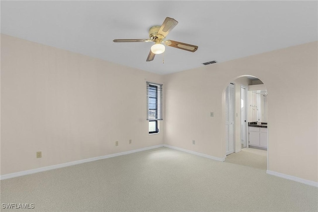 empty room with a ceiling fan, visible vents, baseboards, arched walkways, and light colored carpet