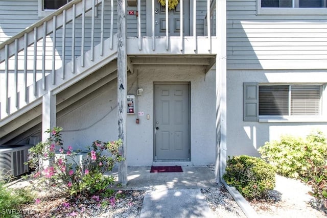 view of exterior entry featuring central air condition unit and stucco siding