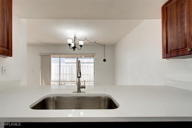 kitchen with a notable chandelier, a textured ceiling, light countertops, and a sink