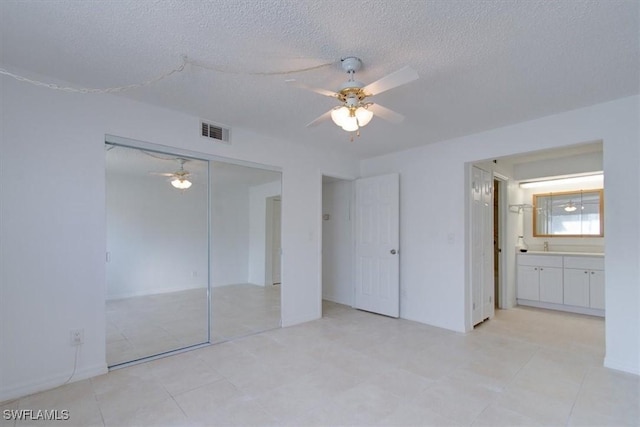 unfurnished bedroom with visible vents, connected bathroom, a closet, a textured ceiling, and a ceiling fan