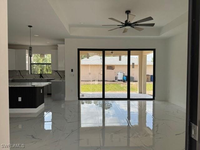 doorway to outside with marble finish floor, a raised ceiling, ceiling fan, and a sink