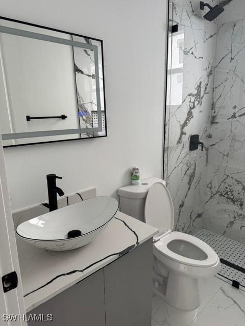 bathroom with a marble finish shower, toilet, marble finish floor, and vanity