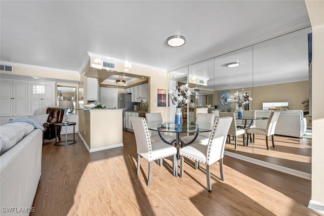 dining area featuring wood finished floors, visible vents, and ornamental molding