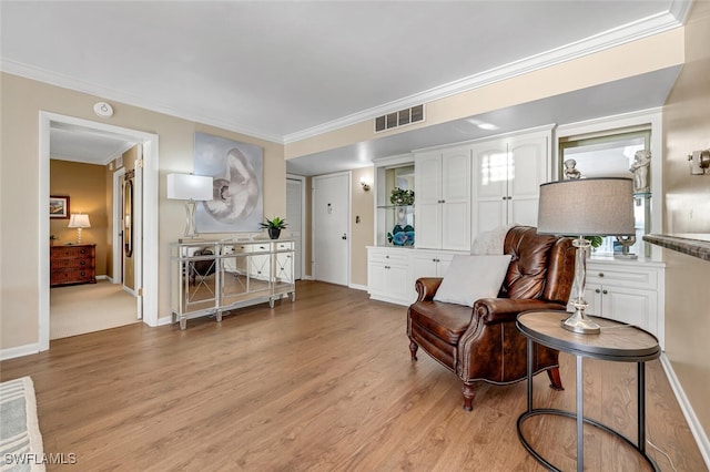 sitting room with baseboards, visible vents, light wood finished floors, and ornamental molding