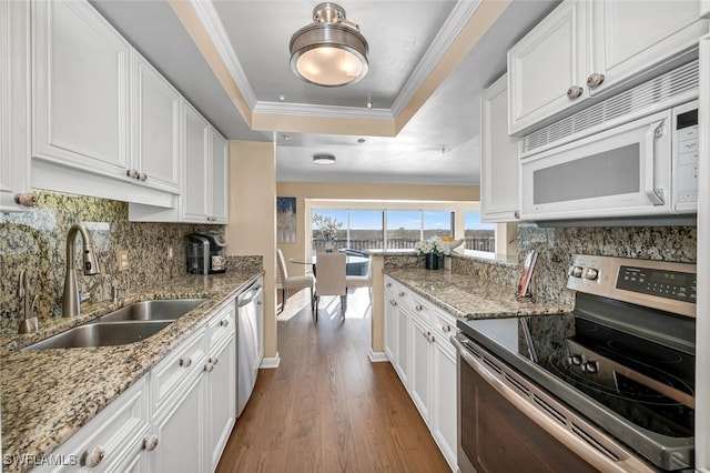 kitchen with a sink, a tray ceiling, white cabinetry, stainless steel appliances, and crown molding