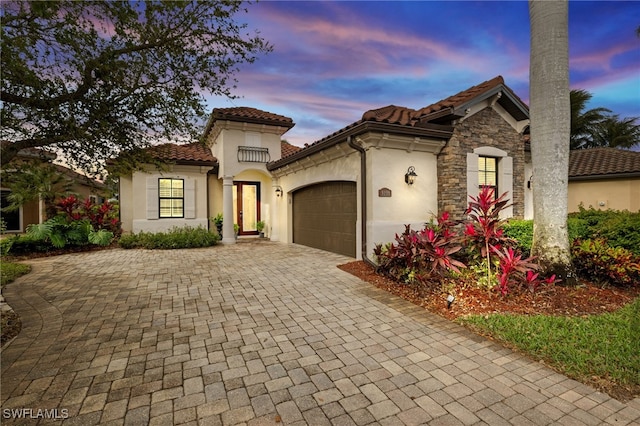 mediterranean / spanish house featuring a tile roof, stucco siding, decorative driveway, a garage, and stone siding