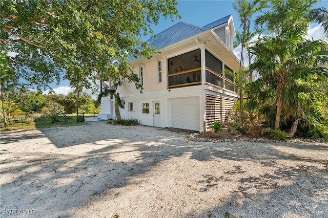 view of property exterior featuring a ceiling fan, gravel driveway, an attached garage, a sunroom, and metal roof