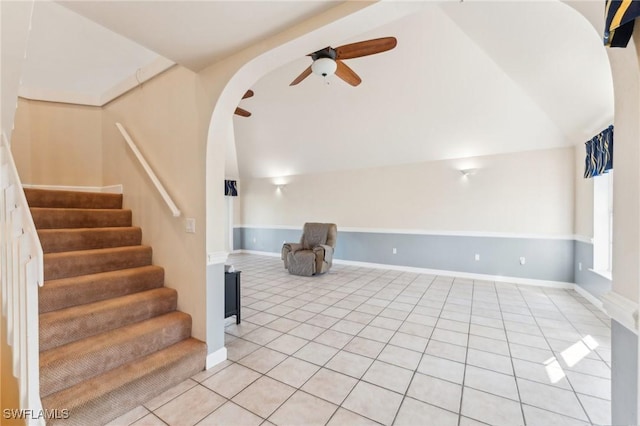 interior space featuring a ceiling fan, arched walkways, light tile patterned floors, baseboards, and stairs