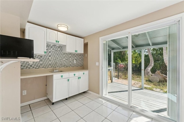 kitchen with tasteful backsplash, light countertops, light tile patterned floors, white cabinets, and a sink