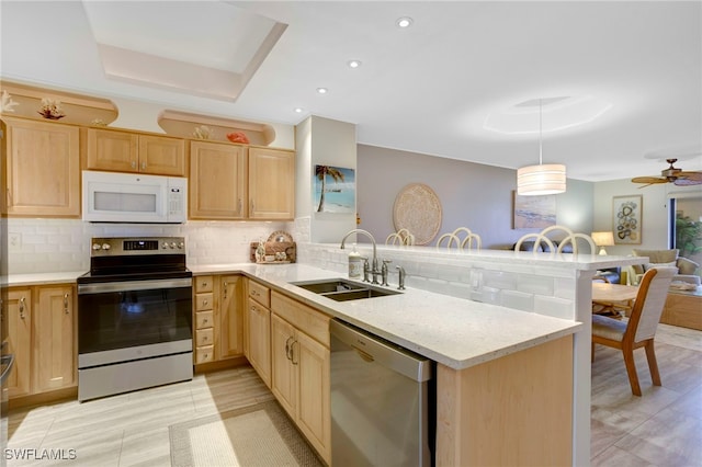 kitchen featuring a peninsula, a sink, decorative backsplash, light brown cabinetry, and stainless steel appliances