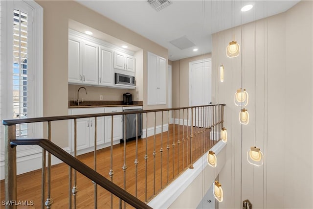 hallway with visible vents, an upstairs landing, a sink, wood finished floors, and recessed lighting