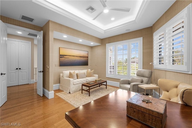 living room featuring light wood finished floors, visible vents, a tray ceiling, and ceiling fan