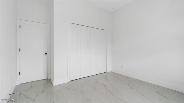 unfurnished bedroom with a closet, baseboards, and marble finish floor