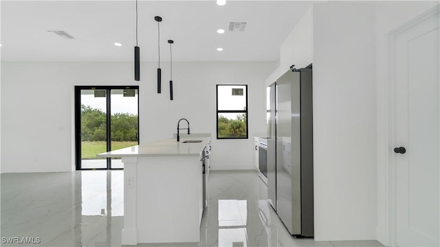 kitchen featuring marble finish floor, a sink, freestanding refrigerator, white cabinets, and a healthy amount of sunlight