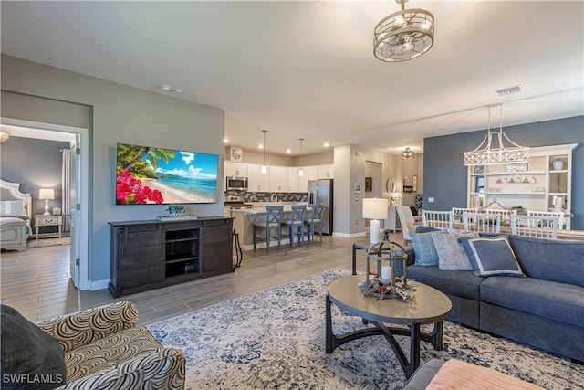 living room with visible vents, baseboards, recessed lighting, a notable chandelier, and light wood-type flooring