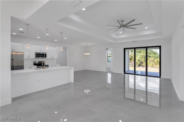 unfurnished living room featuring a raised ceiling, recessed lighting, ceiling fan with notable chandelier, and visible vents