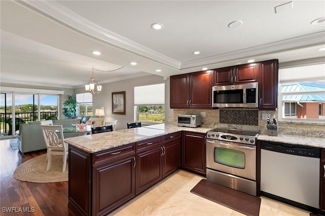 kitchen featuring light stone counters, a peninsula, appliances with stainless steel finishes, crown molding, and backsplash