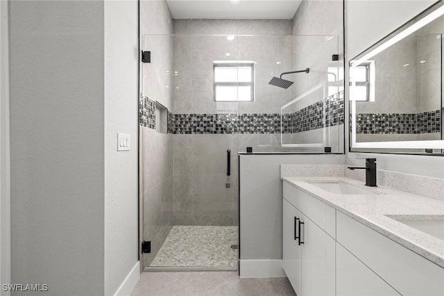 full bathroom featuring a sink, baseboards, a stall shower, and double vanity