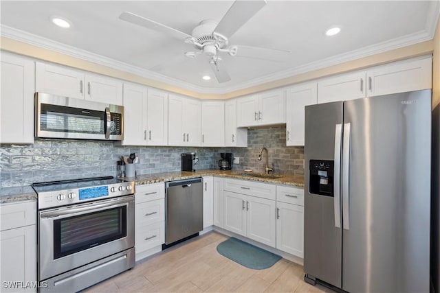 kitchen with a sink, stainless steel appliances, light stone counters, and white cabinets