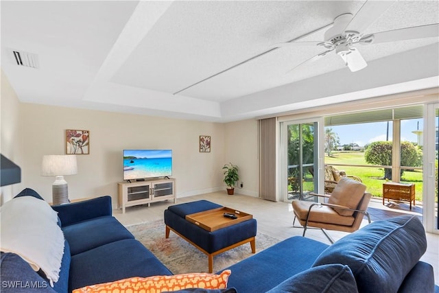 living room with a tray ceiling, visible vents, baseboards, and a ceiling fan