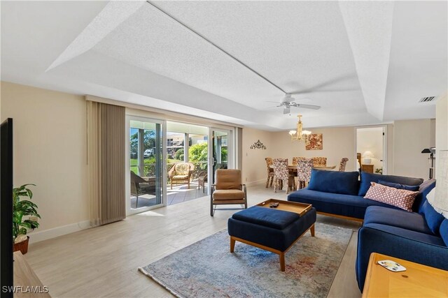 living room featuring visible vents, baseboards, a tray ceiling, wood finished floors, and a textured ceiling