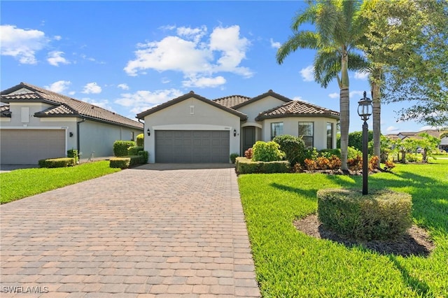 mediterranean / spanish home with a front lawn, a tiled roof, stucco siding, decorative driveway, and an attached garage