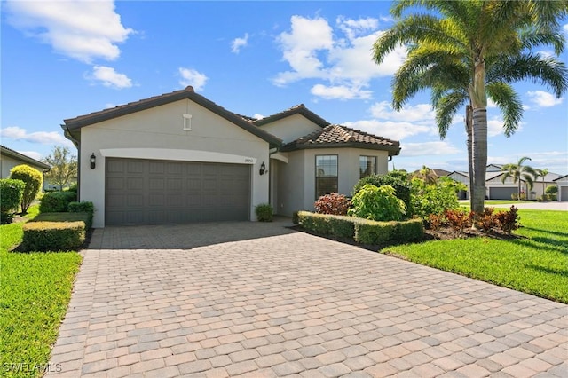 mediterranean / spanish-style home with stucco siding, a front lawn, a tile roof, decorative driveway, and an attached garage