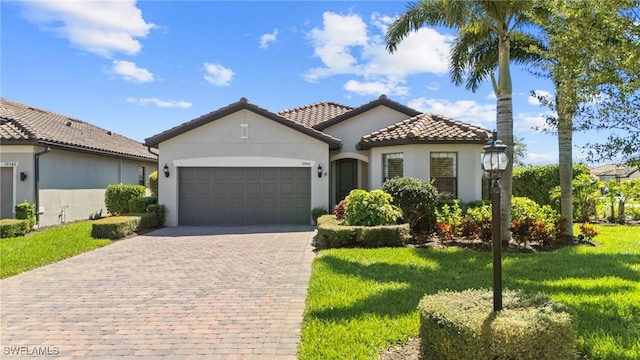 mediterranean / spanish home with stucco siding, decorative driveway, a front yard, an attached garage, and a tiled roof