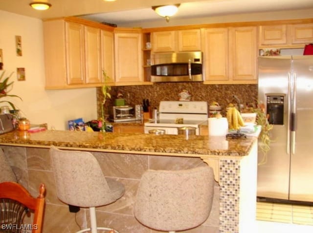 kitchen with a peninsula, stone countertops, light brown cabinetry, stainless steel appliances, and a kitchen breakfast bar