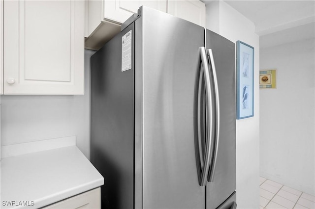 kitchen with tile patterned flooring, white cabinetry, freestanding refrigerator, and light countertops